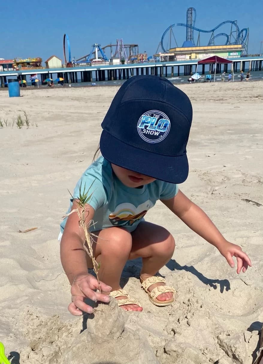 Young PLO Show fan in the navy snapback playing in the sand at Galveston Beach